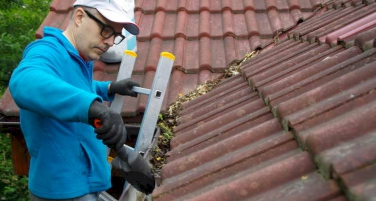 person cleaning gutters of roof