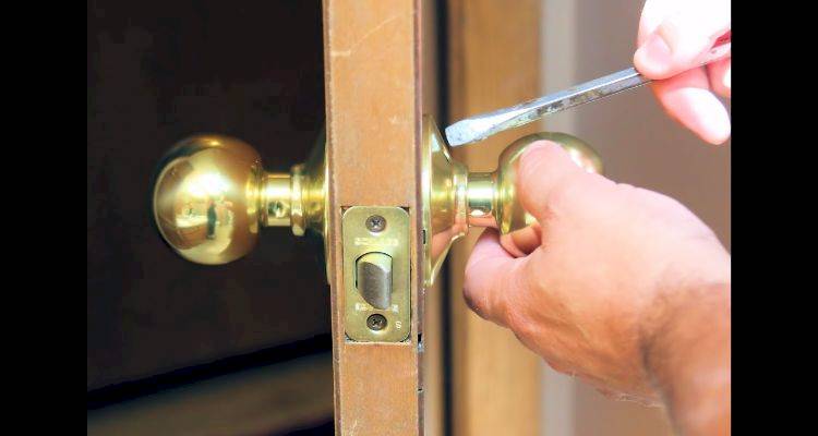 locksmith cost guide — a simple door lock being removed with a screwdriver by a tradesperson