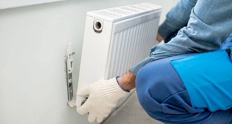 central heating installation cost guide — tradesperson fitting a new radiator to a radiator wall fixture