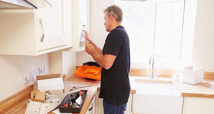 central heating installation cost guide — tradesperson installing a new boiler in a kitchen cabinet