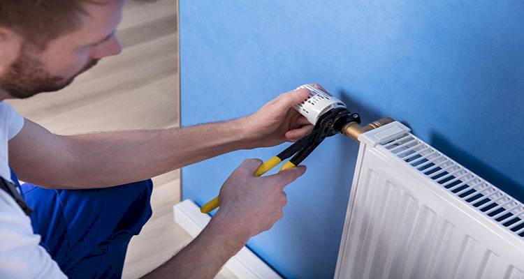 central heating installation cost guide — tradesperson fitting the valve on a radiator