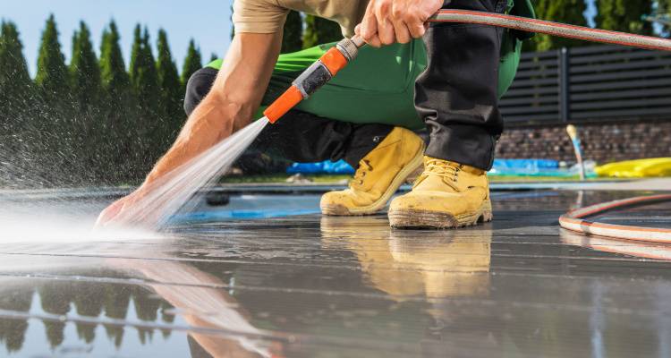 person crouched jet washing patio