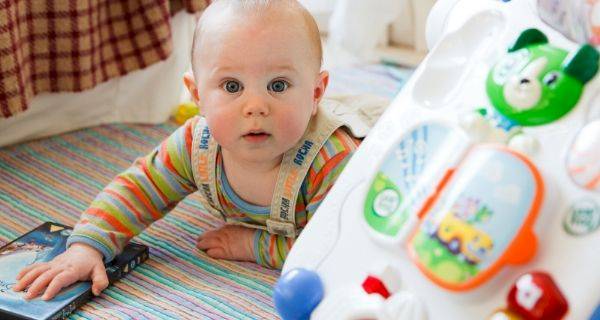 wide eyed baby crawling on floor with baby toys