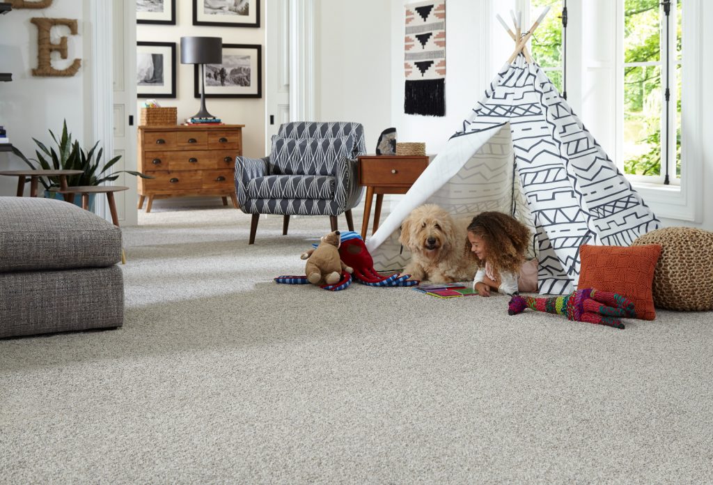 Child and dog lay in tent in living room on carpet