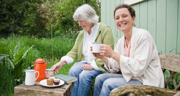 two ladies sitting outside a shed having a cup of tea