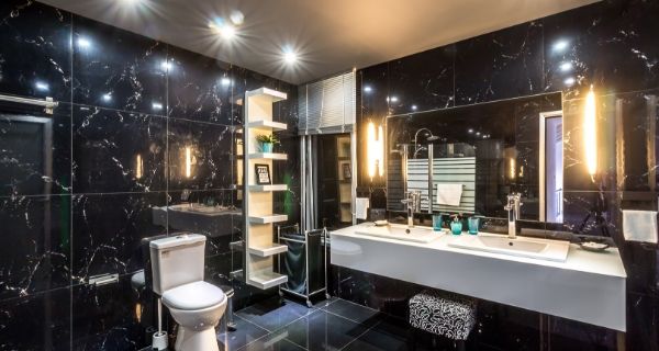 black tile bathroom that is a wet room and has lights around a large mirror
