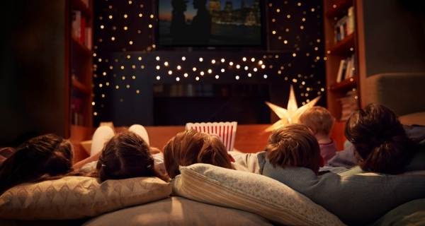 Family lay on sofa looking at TV with fairy lights for movie night